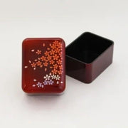 Red lacquered small accessory case with gold cherry blossom design on a traditional Japanese background